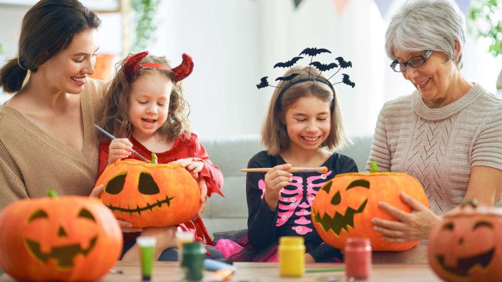 Familia disfrazada pintando calabazas en casa como parte de juegos niños para Halloween