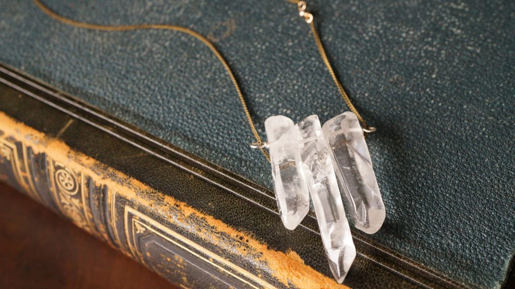 Colgante artesanal con cuarzos transparentes sobre libro antiguo, producto espiritual de tienda de regalos en Alicante