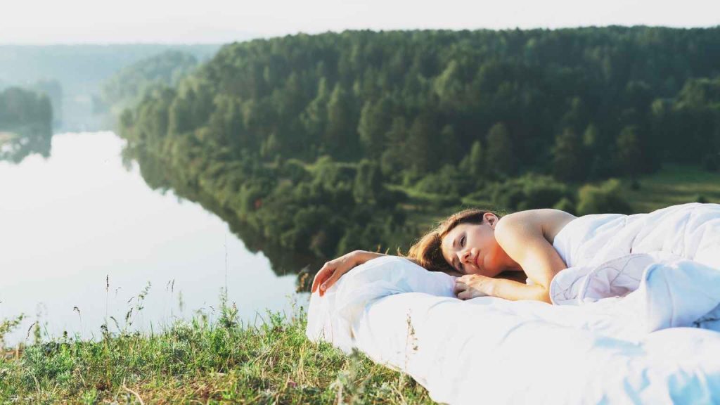 Mujer descansando al aire libre junto a un río, simbolizando el impacto positivo de la naturaleza en la salud mental, tema abordado por psicólogos en Valencia.