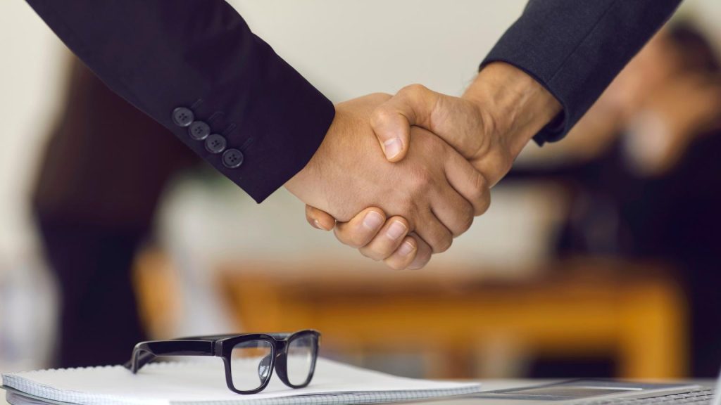 Business agreement with handshake between two professionals in office, recruitment solutions partnership