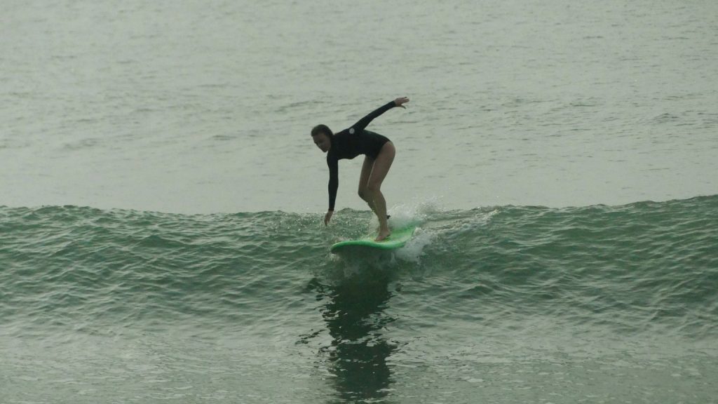 Beginner in a surf class on a longboard with instructor guiding posture on a small wave
