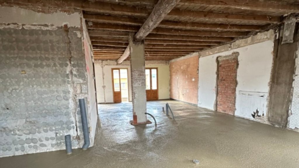 Interior de vivienda en proceso de Reformas integrales con techos de vigas de madera a la vista y solera de cemento húmeda en el suelo.