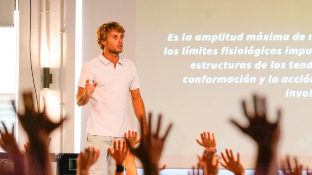 Instructor guiando una formación presencial sobre entrenamiento personal frente a un grupo con manos levantadas.