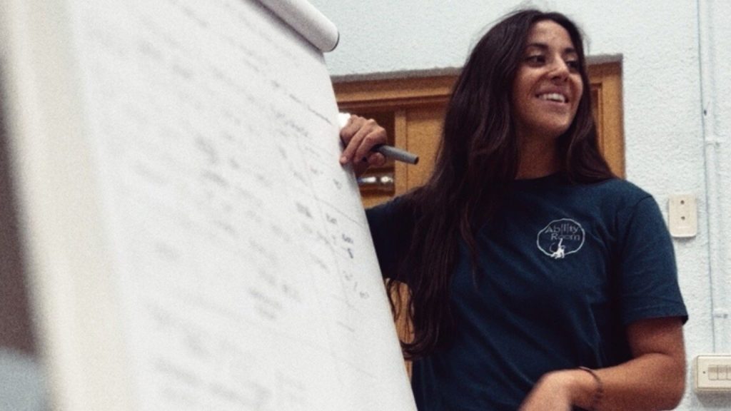 Formadora de Ability Room explicando una planificación de entrenamiento personal en una pizarra durante una clase teórica.