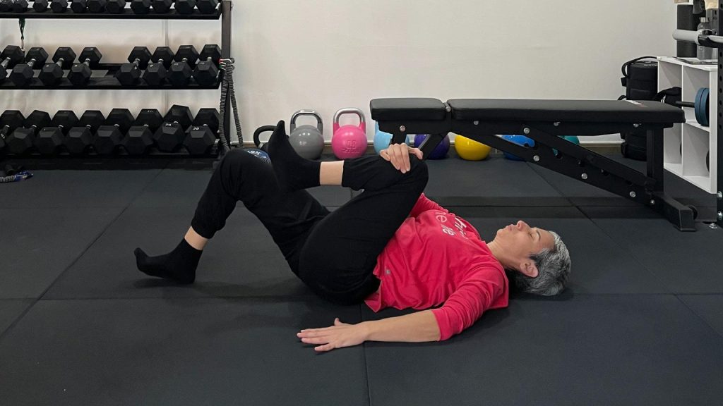 Dona realitzant un exercici de mobilitat de maluc i esquena en un centre d’entrenament amb material de força i treball funcional orientat a la salut