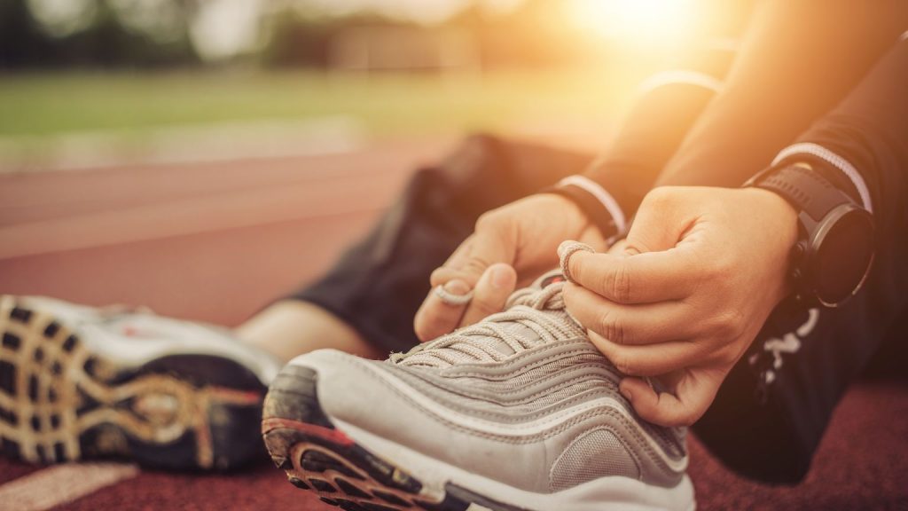 Persona atándose zapatillas técnicas sobre pista de atletismo al atardecer, preparándose para entrenar con productos deportivos esenciales.