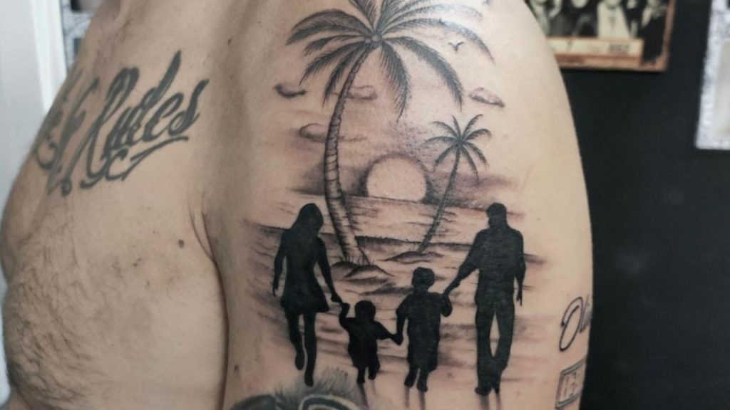 Tattoo studio profesional realizando tatuaje realista en blanco y negro con escena familiar en la playa