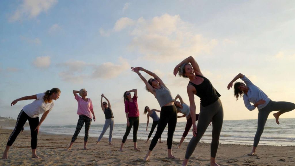 Grupo de entrenamiento al aire libre en Málaga con personas entrenando en la playa, guiadas por un entrenador profesional en un ambiente de comunidad y bienestar.