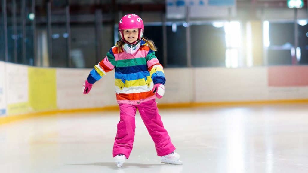 Niña patinando con casco y protecciones en una escuela de patinaje infantil, practicando deporte y hábitos saludables desde pequeña.