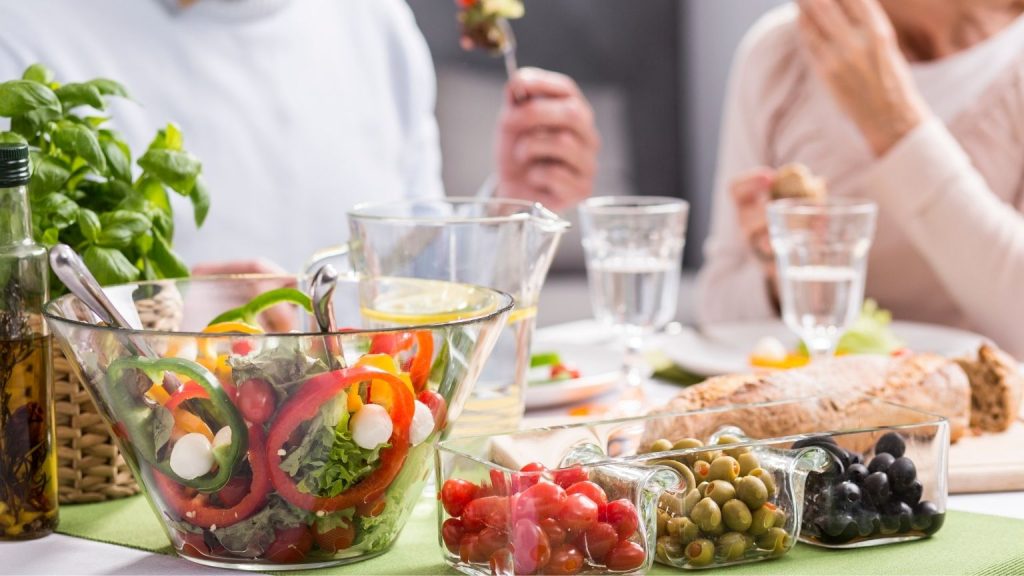 Mesa con ensalada fresca, verduras, pan integral y alimentos naturales compartidos, ejemplo de hábitos saludables y alimentación equilibrada en el día a día.
