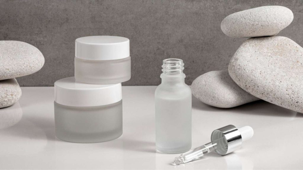 Productos de cuidado facial naturales en envases neutros junto a piedras suaves sobre fondo gris minimalista.