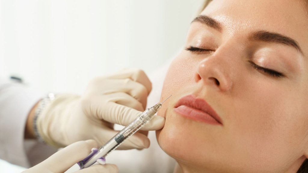 Mujer recibiendo tratamiento de medicina estética facial con inyección realizada por profesional sanitario en clínica estética