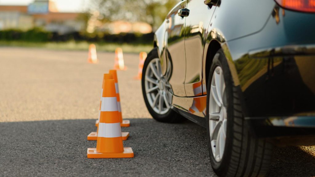 Escuela de conducción profesional realizando prácticas de aprendizaje con conos y vehículo en zona de entrenamiento